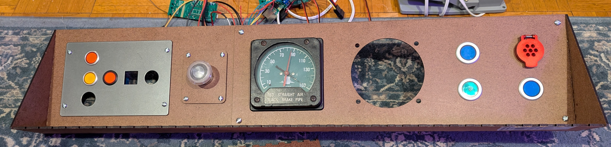Wide and short hardboard assembly, containing buttons and an air gauge, lying on a blue patterned rug.