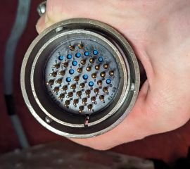 A hand holding a large circular electrical plug containing many metal pins